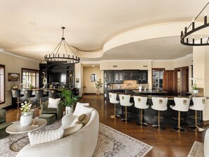 Amplia sala de estar con techo curvo, barra con taburetes altos y cocina con muebles oscuros.