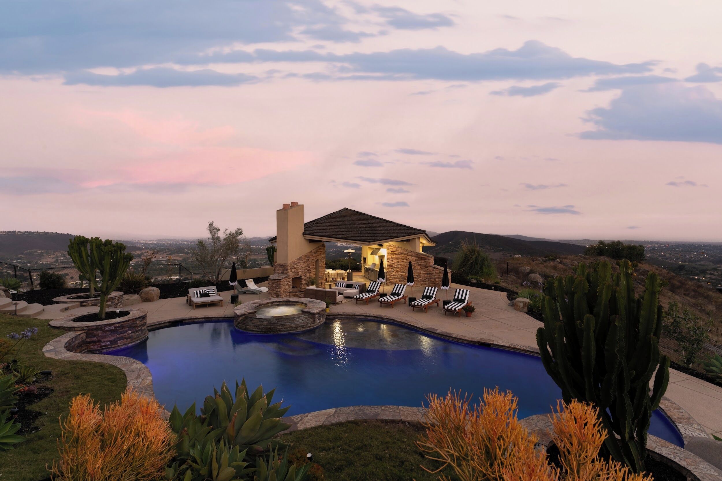 A pool with lounge chairs, a stone building, and a view of the landscape.