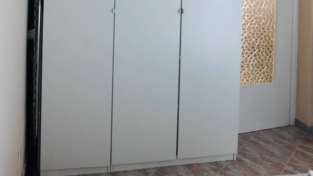 Ein Zimmer mit einem großen, weißen Kleiderschrank, einer Tür mit Muster und einer gewobenen Leuchte.