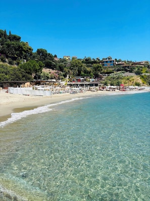 Una spiaggia con acqua cristallina, ombrelloni e edifici sullo sfondo.