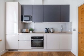 A compact kitchen with white cabinets, a microwave, a toaster, a coffee maker, and an oven. - Prime Fitzrovia Location - Stylish 1BR (London)