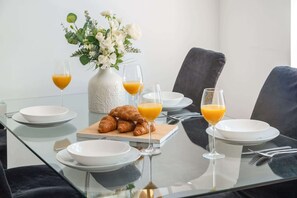 Ein Frühstückstisch mit Croissants, Orangensaft und einer Blumenvase auf einer Glastischplatte.