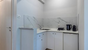 A compact kitchen with a sink, a coffee maker, and a kettle on the counter.