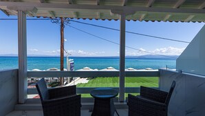 A balcony with wicker chairs, a small table, and a view of the sea and distant mountains.
