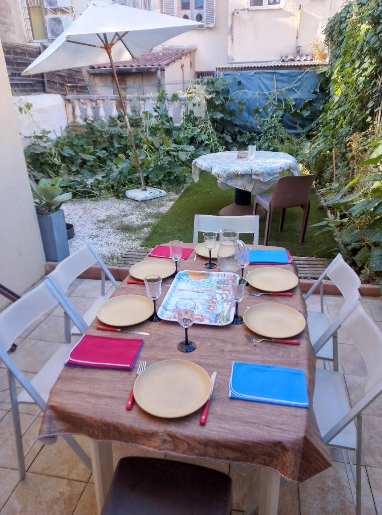 Een buitenontbijtplaats met een tafel voor zes personen, omringd door stoelen, en een kleine ronde tafel met tafelkleed.