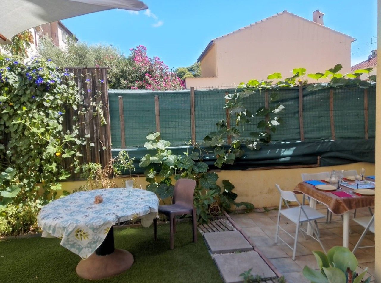 A patio with a table and chairs, surrounded by greenery and a fence.