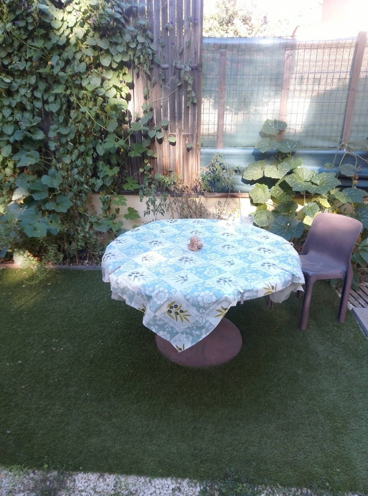 A round table with a floral tablecloth, a chair, and a small decorative item on the table.