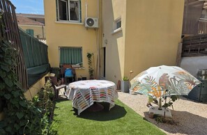 Eine kleine Terrasse mit Tisch, einem Tischläufer mit Muster, einem Stuhl und einem Sonnenschirm.
