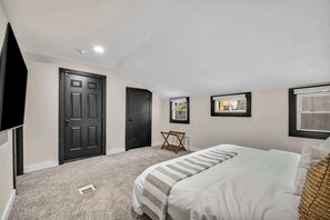 A bedroom with a bed, two doors, a window, and a small table. - Near Tremont - 4BR - Sleeps 15 - Xbox (Cleveland)
