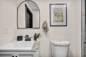 A bathroom with a white sink, a mirror, a framed guest check, and a toilet. - Near Tremont - 4BR - Sleeps 15 - Xbox (Cleveland)