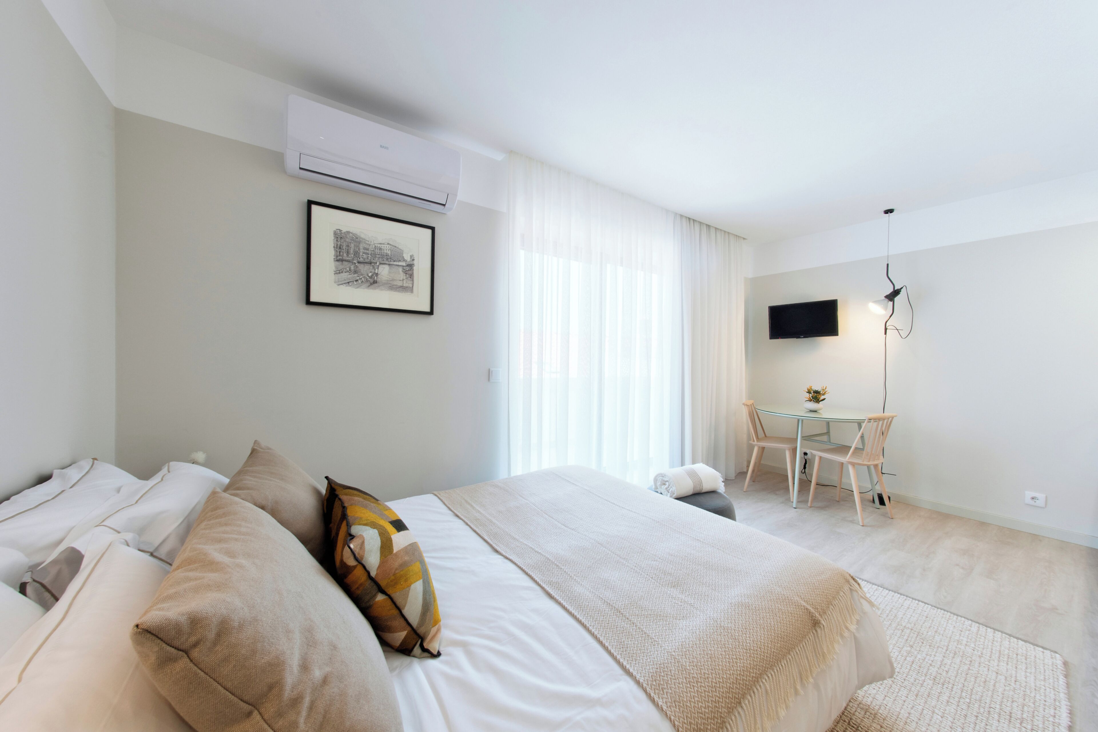 A hotel room with a bed, a desk, a chair, a television, and an air conditioning unit.
