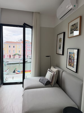 Habitación de hotel con cama, ventana con vistas a edificios y barcos, y equipo de aire acondicionado.