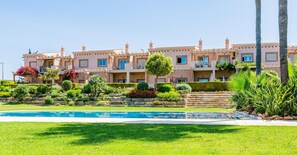 A multi-story hotel with a swimming pool, landscaped gardens, and palm trees. - Casa Colina – Spacious Villa w/ Pool Near Beach! (Albufeira)