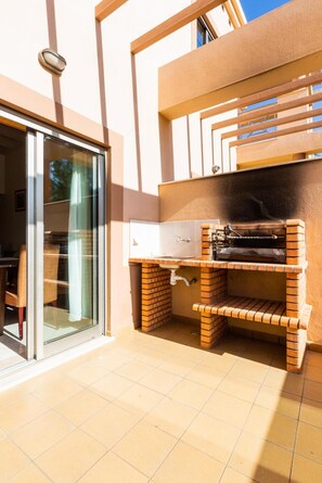 A patio area with a brick barbecue grill, a glass door entrance, and a tiled floor. - Casa Colina – Spacious Villa w/ Pool Near Beach! (Albufeira)