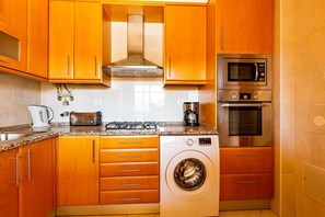 A kitchen with wooden cabinets, a stainless steel microwave, an oven, a washing machine, and a gas stove. - Casa Colina – Spacious Villa w/ Pool Near Beach! (Albufeira)