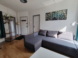 Ein modernes Wohnzimmer mit einem Ecksofa, einem weißen Couchtisch, einer Stehlampe und einem Pfau-Motiv an der Wand.