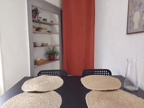 Ein Esstisch mit zwei gewebten Platzsets, einer klaren Vase und einem Regal mit Pflanzen und Körben.