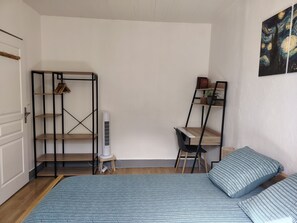 Ein Schlafzimmer mit einem Bett, einem Schreibtisch und einem Stuhl. Es gibt einen Kleiderschrank mit Regalen sowie eine Heizung.