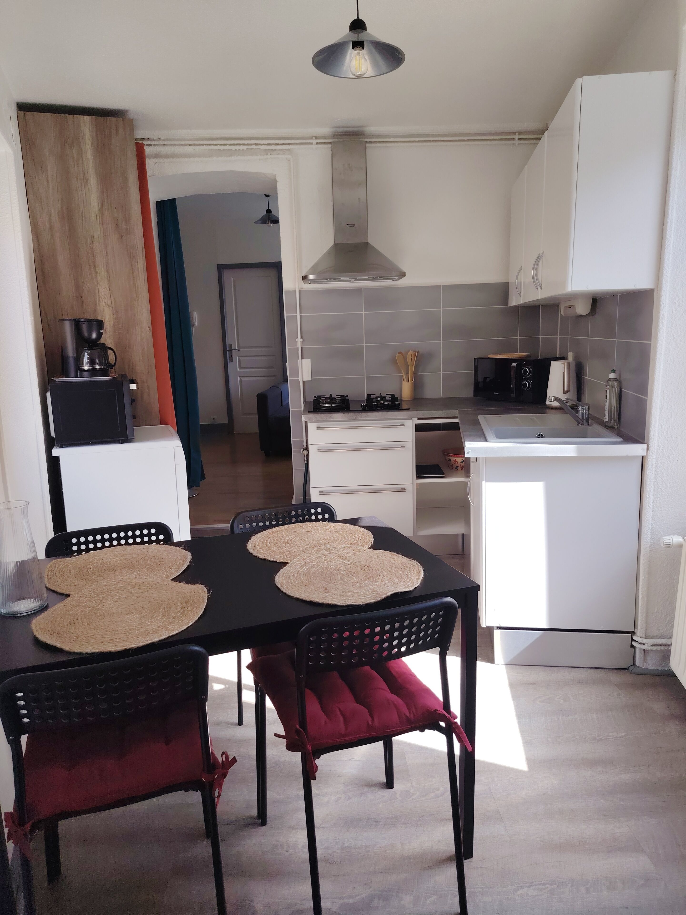 Eine moderne Küche mit Essbereich, ausgestattet mit einem schwarzen Tisch, gewobenen Platzsets, schwarzen Stühlen und einem weißen Kühlschrank.