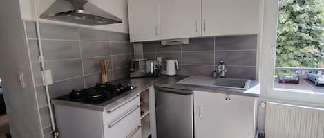 Une cuisine de taille réduite, équipée d’une cuisinière à gaz, d’un évier et de meubles blancs.