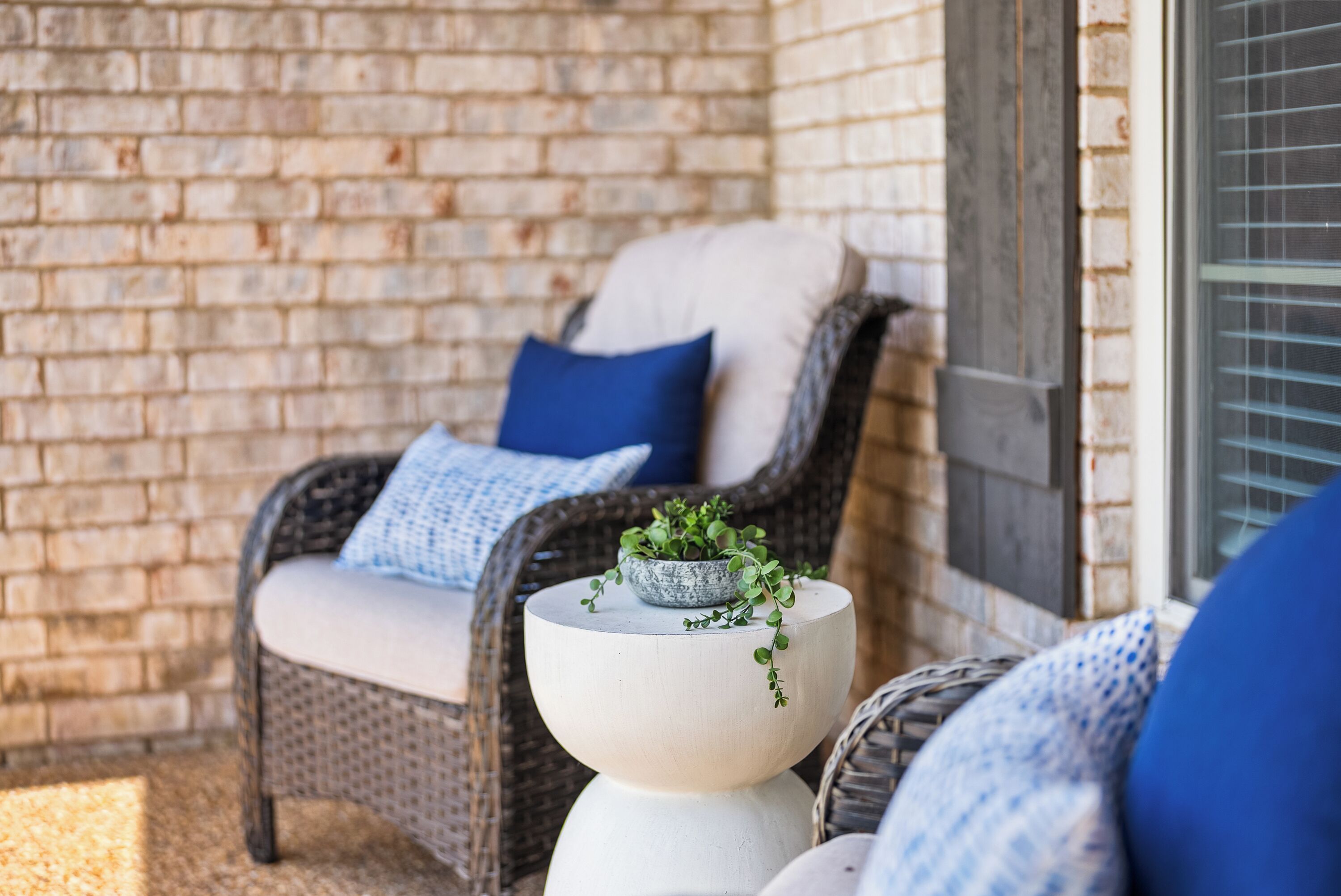 A wicker chair with a cushion and a small potted plant on a white pedestal.