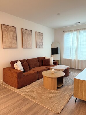 Ein modernes Wohnzimmer mit einem braunen Ecksofa, einem runden Couchtisch und einem wandmontierten Flachbildfernseher.