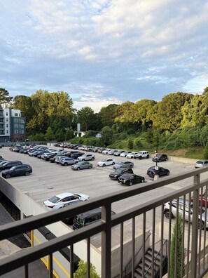 Ein Parkplatz mit mehreren Autos, ein Gebäude im modernen Stil und Blick auf Bäume und Grünflächen.