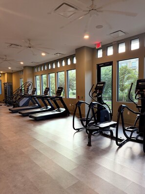 Ein Fitnessraum mit Laufbändern, Crosstrainern und einem Deckenventilator.