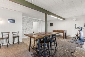 A room with a wooden table, bar stools, a ping pong table, and a stationary bike. - Haliburton Lakefront Escape with Hot Tub, Fire Pit, Sauna & BBQ (Algonquin Highlands)