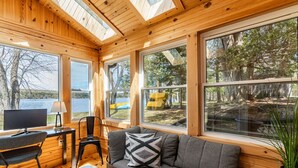 Interno di una cabina con arredamento in legno, un divano, una scrivania con una sedia e ampie finestre che offrono vista sul panorama esterno.