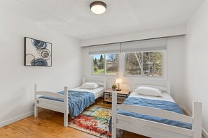 A room with two single beds, a small table with a lamp, a colorful rug, and a painting on the wall. - Haliburton Lakefront Escape with Hot Tub, Fire Pit, Sauna & BBQ (Algonquin Highlands)
