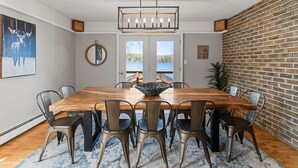 Una sala da pranzo con tavolo in legno, sedie in metallo, un lampadario e vista attraverso una porta vetrata.
