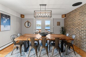 A dining room with a wooden table, metal chairs, a chandelier, and a view through a glass door. - Haliburton Lakefront Escape with Hot Tub, Fire Pit, Sauna & BBQ (Algonquin Highlands)