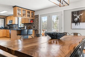 A modern kitchen with wooden cabinets, a stone backsplash, and a dining area with a wooden table and chairs. - Haliburton Lakefront Escape with Hot Tub, Fire Pit, Sauna & BBQ (Algonquin Highlands)