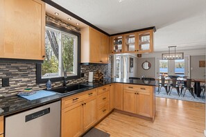 A modern kitchen with wooden cabinets, a black countertop, and a view to the outside. - Haliburton Lakefront Escape with Hot Tub, Fire Pit, Sauna & BBQ (Algonquin Highlands)