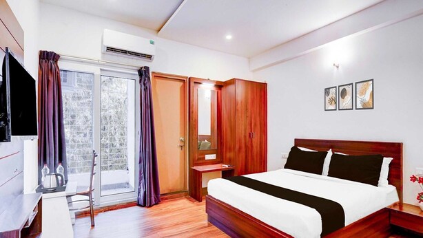 A hotel room with a wooden bed, a desk, a chair, a wardrobe, and a sliding glass door. - Collection O Whitefield Bangalore (Bengaluru)