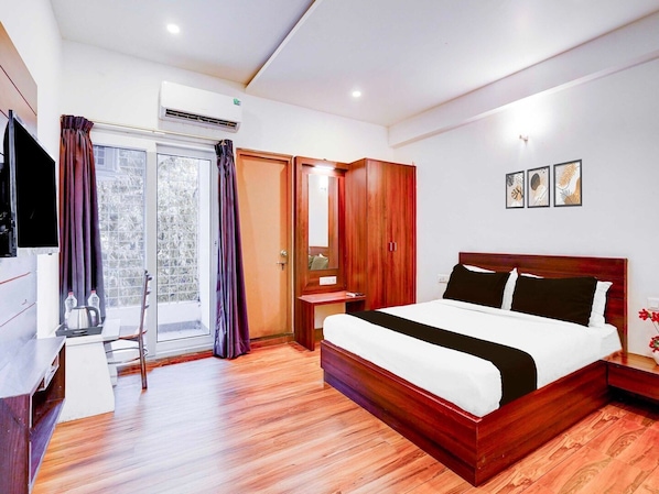 A hotel room with a wooden bed, a desk, a chair, a wardrobe, and a sliding glass door. - Collection O Whitefield Bangalore (Bengaluru)