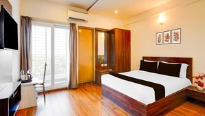 A hotel room with a bed, a desk, a chair, an air conditioning unit, a wardrobe, and a window with curtains. - Collection O Whitefield Bangalore (Bengaluru)