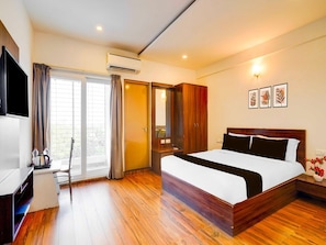 A hotel room with a bed, a desk, a chair, an air conditioning unit, a wardrobe, and a window with curtains. - Collection O Whitefield Bangalore (Bengaluru)