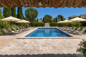 Ein rechteckiger Pool mit Liegestühlen und Sonnenschirmen, umgeben von Pflanzen und Steinböden.