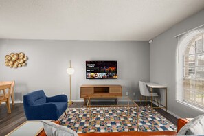 Ein modernes Wohnzimmer mit blauem Sessel, einer Holzeinbauwand, einem gemusterten Teppich und einem an der Wand befestigten Fernseher, der eine Netflix-Sendung zeigt.