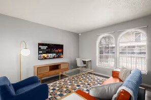 Ein modernes Wohnzimmer mit einer Couch, einem Couchtisch, einem Fernseher und einem gemusterten Teppich.