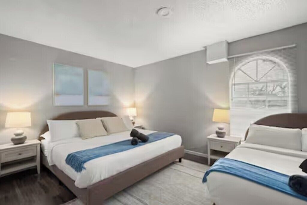 A modern hotel room with a large bed, bedside tables, and a window with blinds.