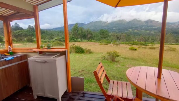 A covered outdoor area with a table and chairs, a small kitchen area, and a view of mountains.