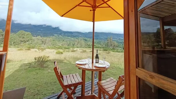 A wooden deck with a table and chairs, a yellow umbrella, and a view of a mountainous landscape.