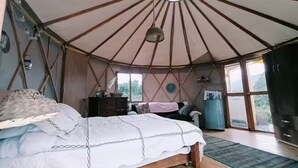 A tent-style room with a bed, dresser, and large windows.