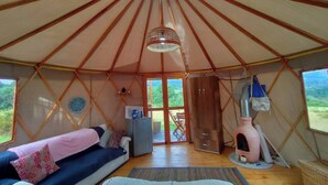 A yurt with a central skylight, a sofa with cushions, a small cabinet, and a pet house.