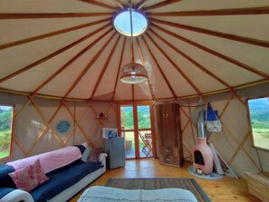A yurt with a central skylight, a sofa with cushions, a small cabinet, and a pet house.