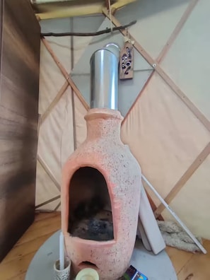 A rustic, clay stove with a chimney, a woven basket, and a metal container on a wooden floor.