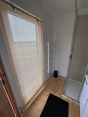 Une salle de bain avec un plancher en bois, un tapis noir, une douche avec une porte en verre et un porte-serviettes blanc.